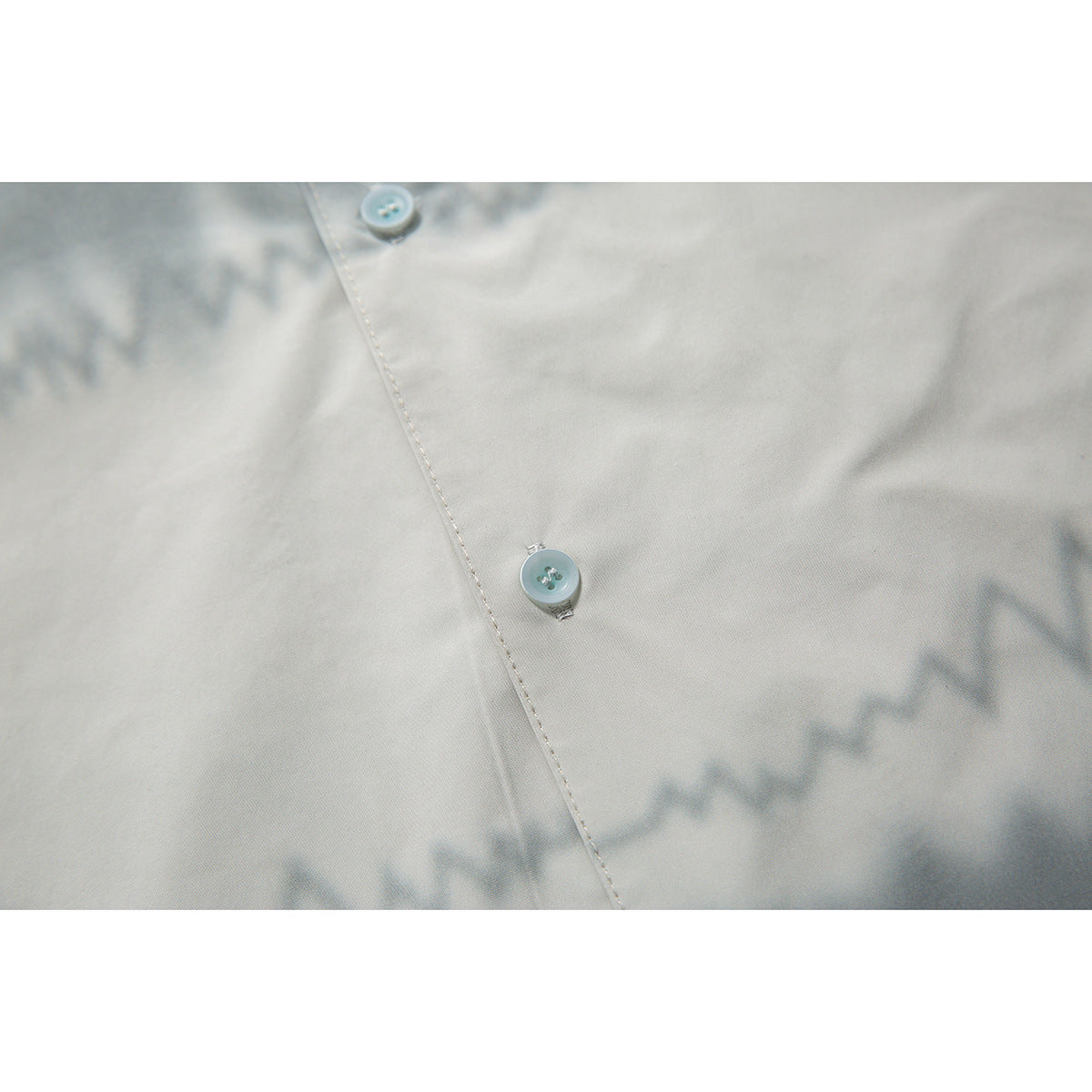 Close-up of two pale blue buttons and stitching on an off-white shirt.