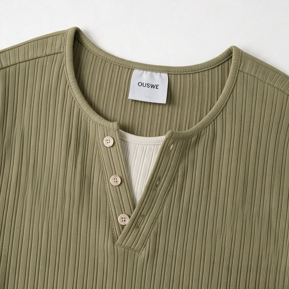 Close-up of an olive ribbed shirt's rounded neckline and button placket with a white inner label.