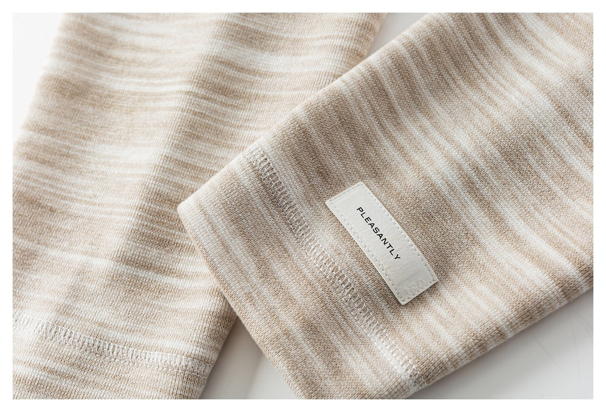 Close-up of a beige heathered knit sleeve cuff with a white sewn label and overlock stitching.