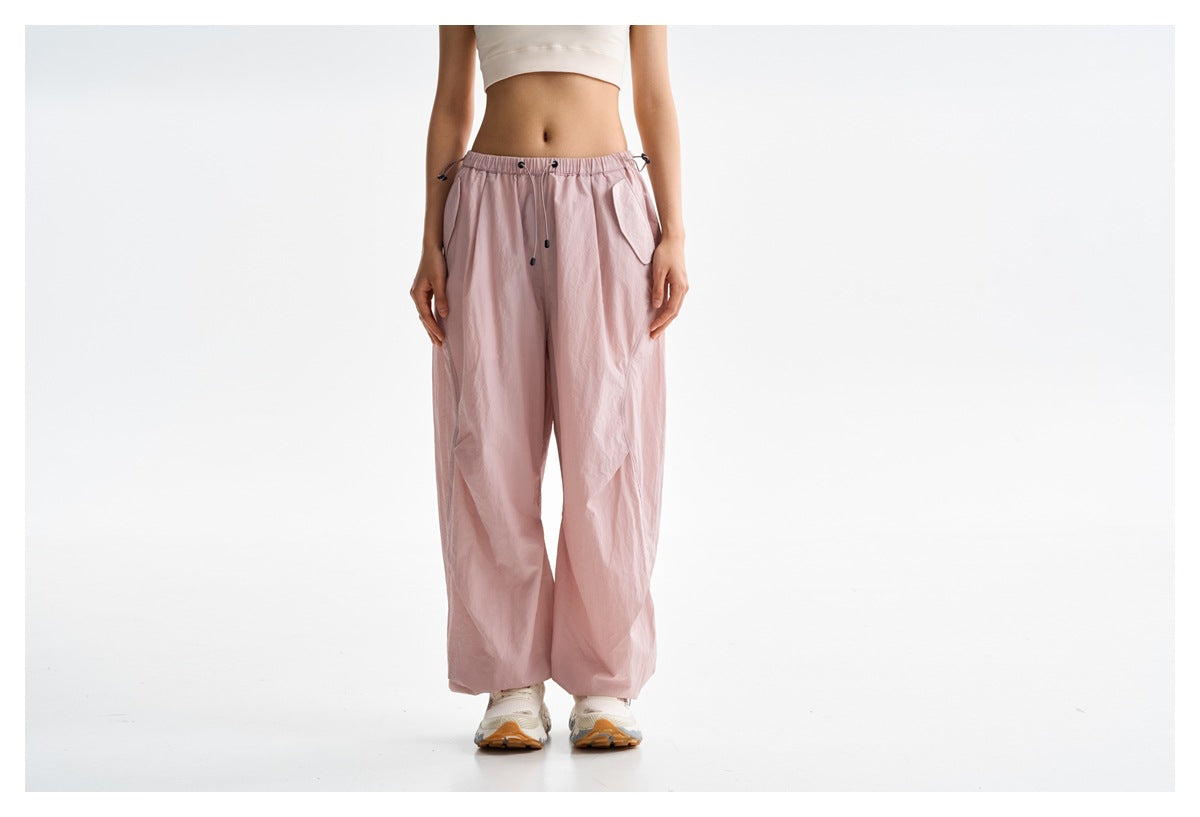 Front view of loose light pink pants with an elastic drawstring waist and flap pockets, worn by a model.