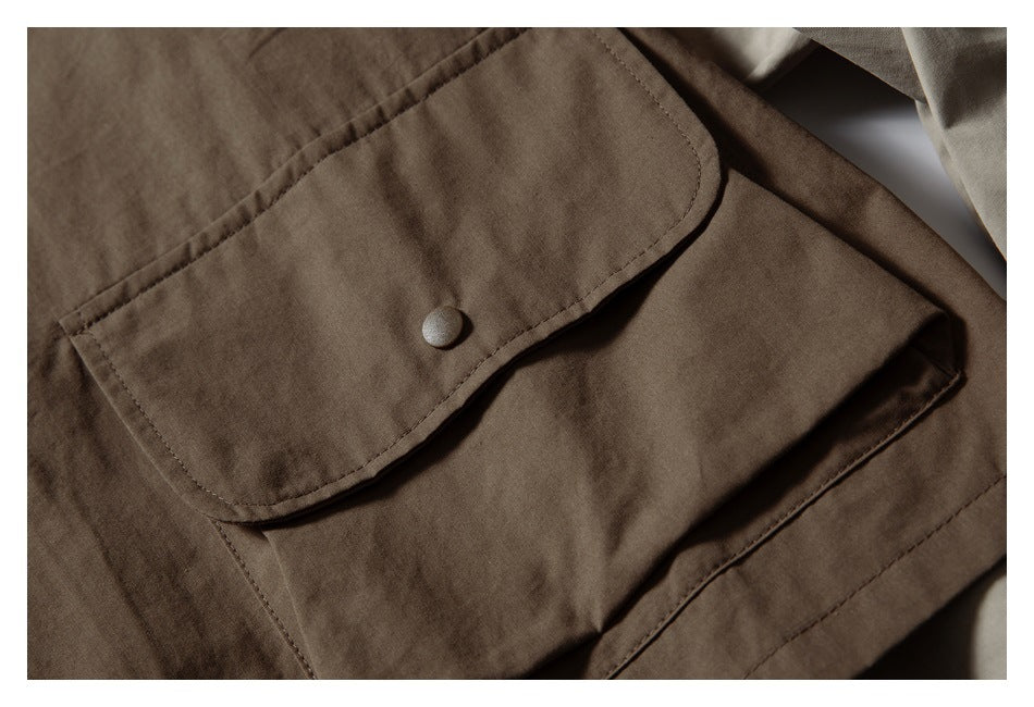 Close-up of a brown overshirt's large flap pocket with a round snap button and visible stitching.