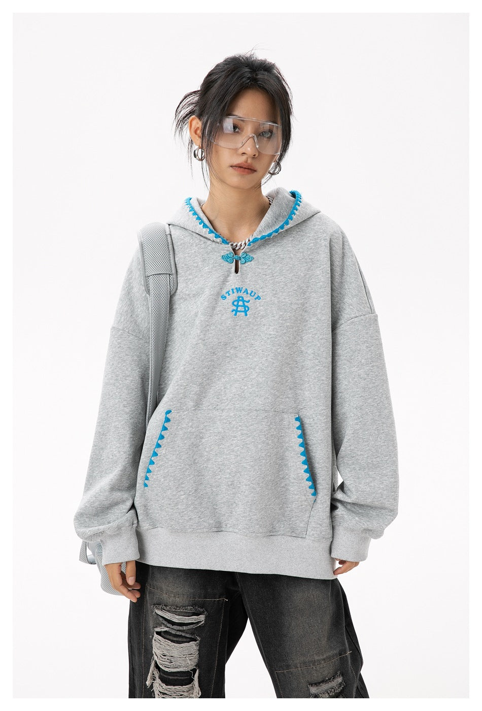 Front view of a model wearing a gray oversized hoodie with blue decorative trim, chest emblem and kangaroo pocket.