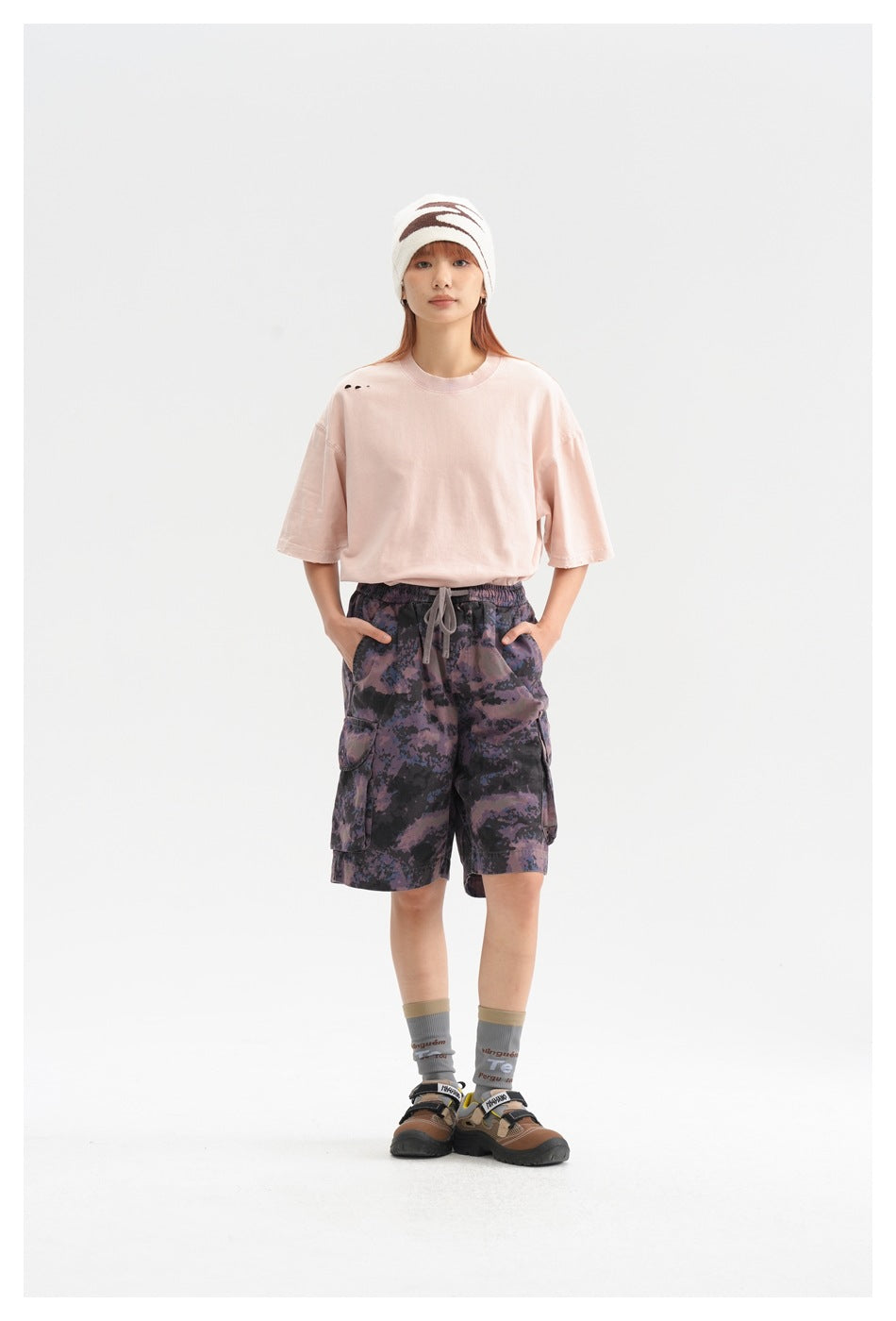 Full-length model in a pale pink oversized T-shirt and purple camouflage cargo shorts with a drawstring waist.
