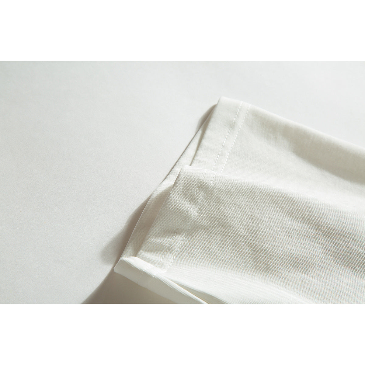 Close-up of the ivory T-shirt sleeve hem and stitching on a light background.