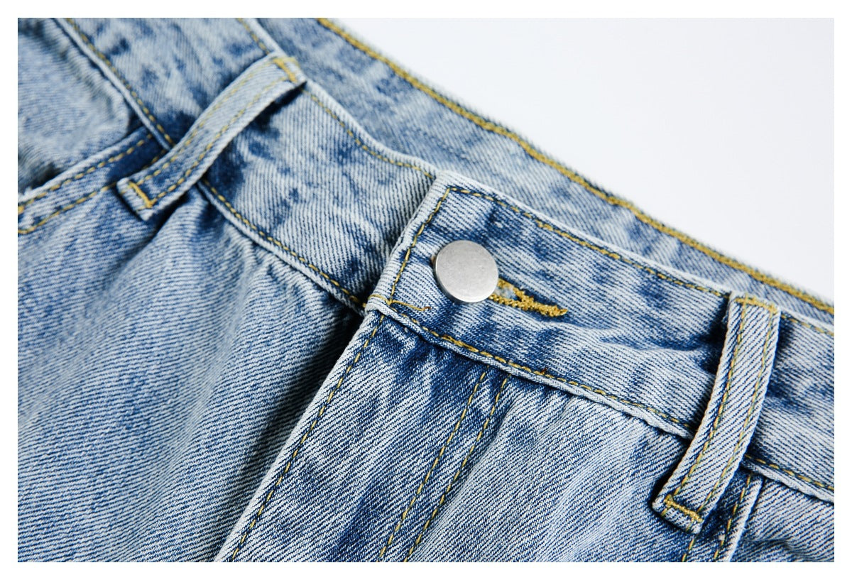 Close-up of the metal button, waistband and belt loops on light-wash jeans.