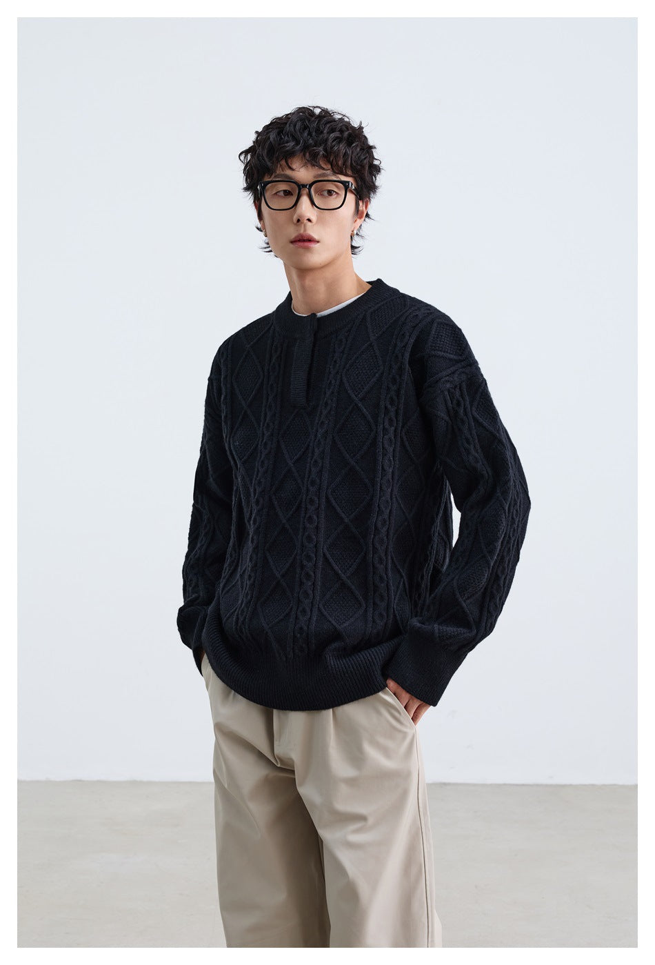 Model wearing a black diamond-pattern cable-knit sweater with ribbed cuffs and hem, paired with beige trousers.