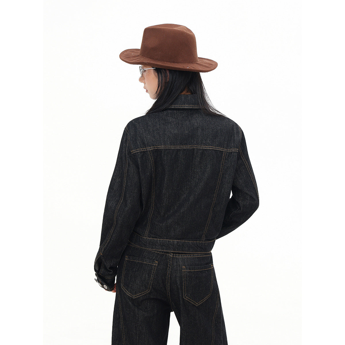 Back view of a model wearing a black denim jacket with contrast stitching and matching jeans.