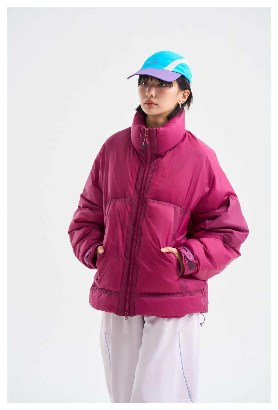 Closer front view of a model in a magenta puffer jacket with a high collar, front zipper, and roomy pockets.