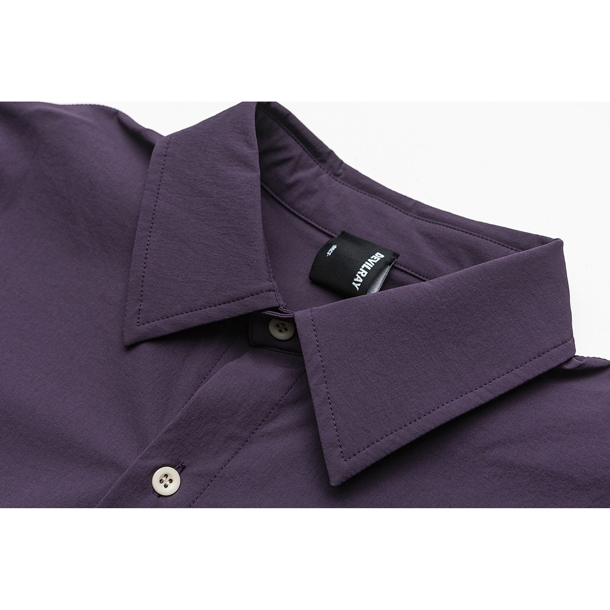 Close-up of a dark plum button-up shirt's pointed collar, cream buttons, stitching, and sewn-in neck label.