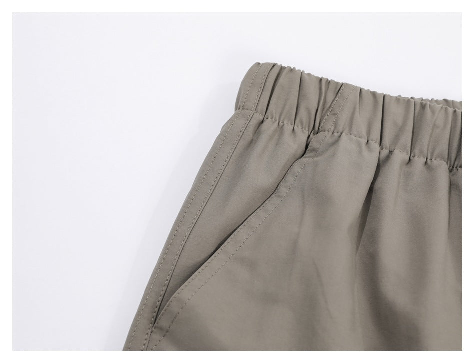 Close-up of taupe trousers showing the elastic waistband and slanted side pocket opening.