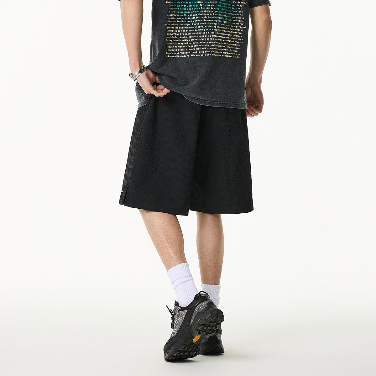 Rear view of a model wearing loose black shorts; the dark T-shirt has a block of English text.