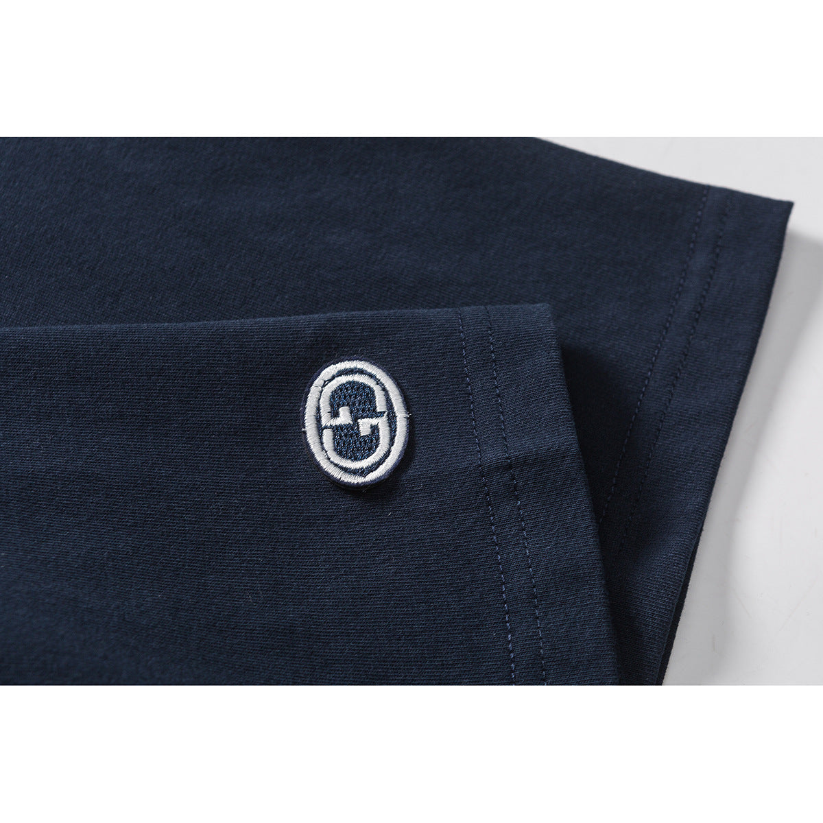Close-up of a white embroidered oval emblem on the navy sleeve of a T-shirt.