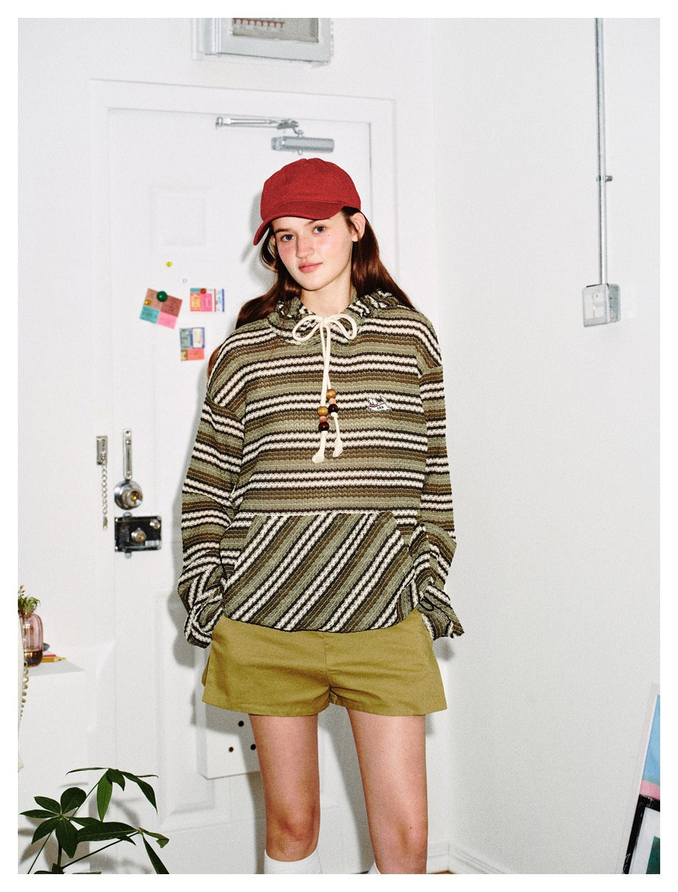 Front view of a model wearing an olive, cream and black striped hoodie with a large pocket and olive shorts.