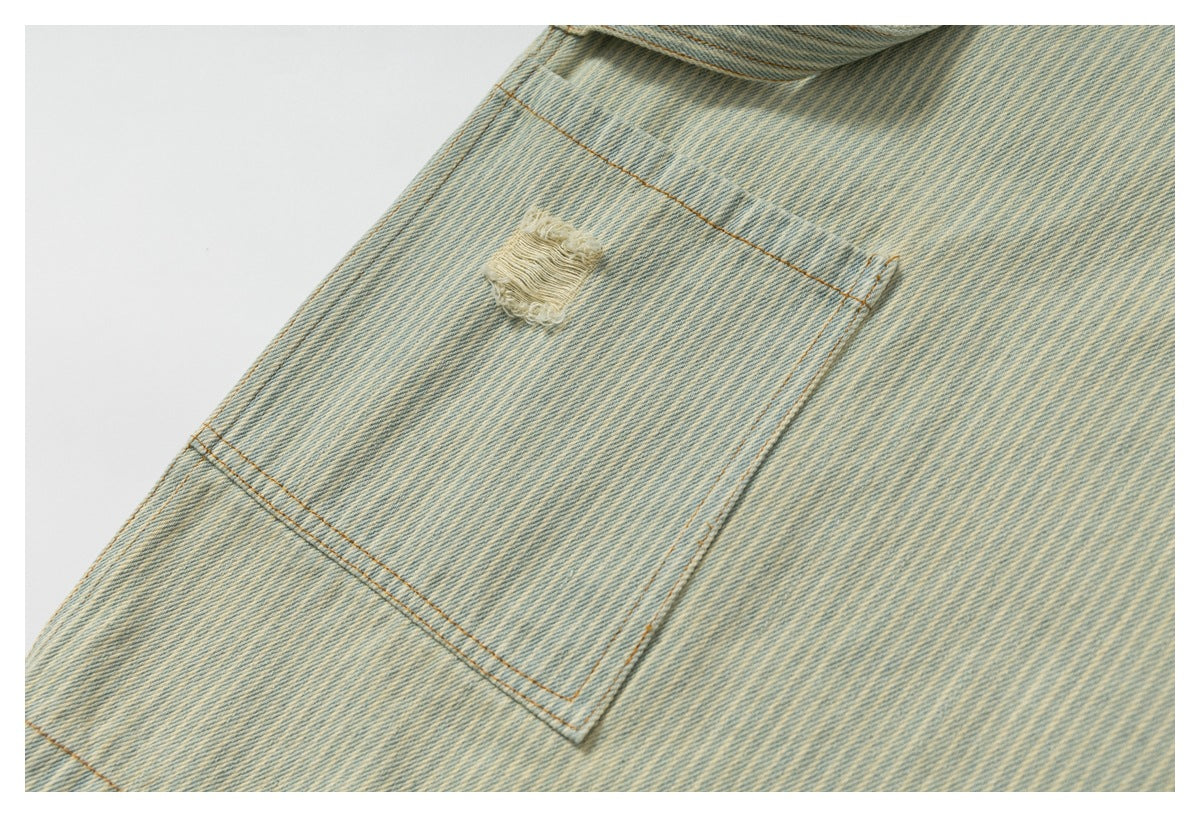 Close-up of a stitched pocket on light washed striped denim with one frayed distressed patch.