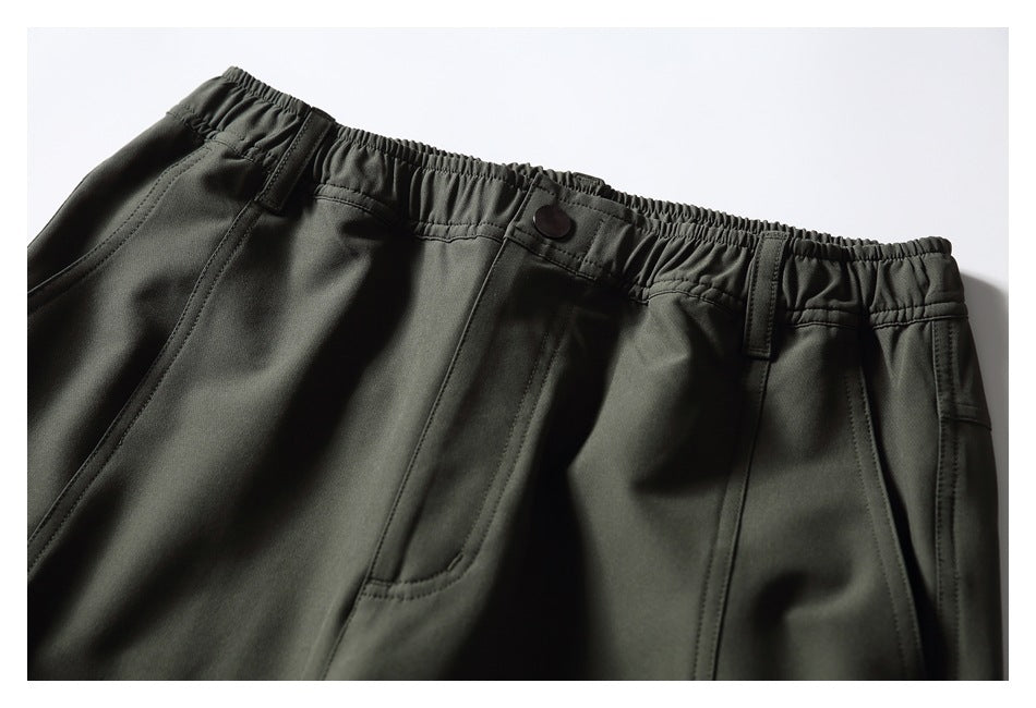 Close-up of dark olive pants showing an elastic waistband, button, belt loops, and front pockets.