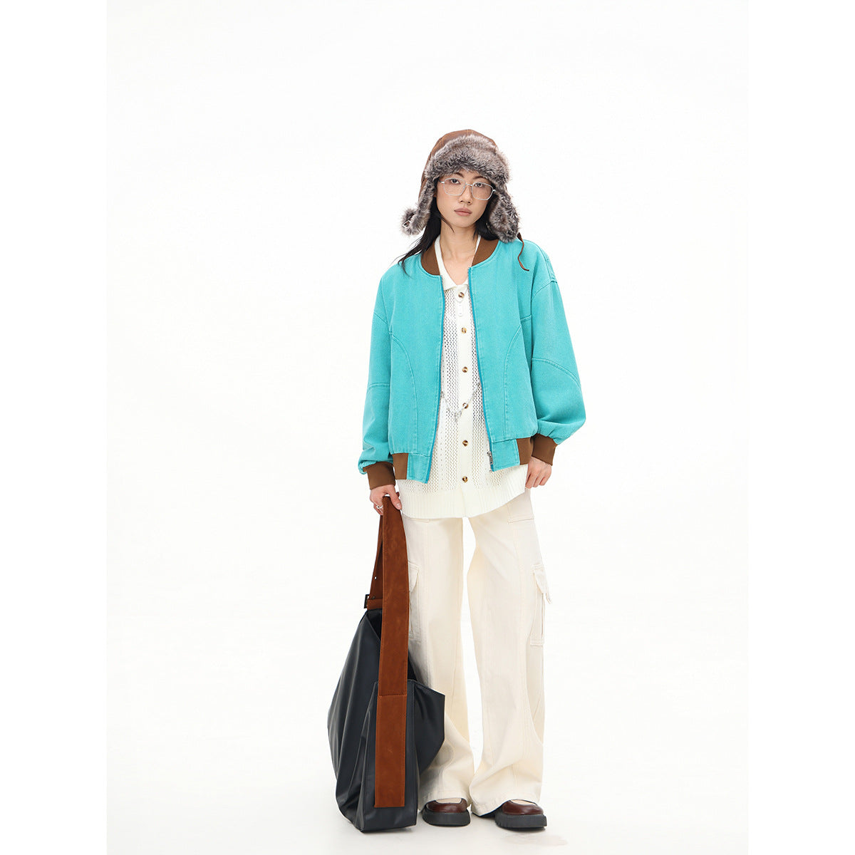 Full-length front view of a model wearing a turquoise bomber jacket with brown trim and cream cargo pants.