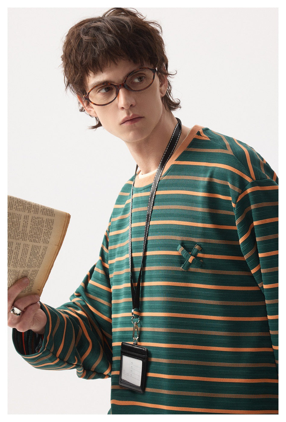 Model wearing a green long-sleeve shirt with orange and dark horizontal stripes and a small chest embellishment.
