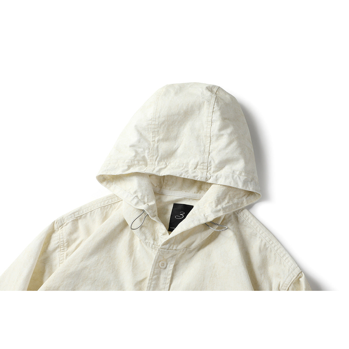 Close-up of an ivory hooded shirt showing the hood, drawcords, collar, and top button of the placket.