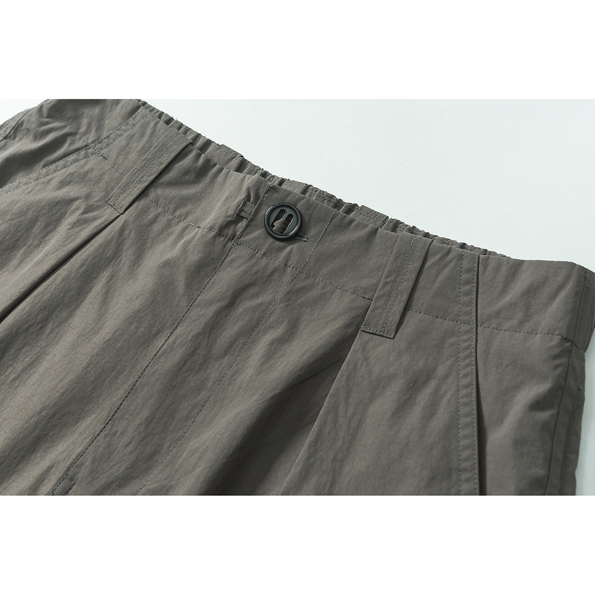 Close-up of gray shorts showing the elastic waistband, belt loops, stitching, and black button.