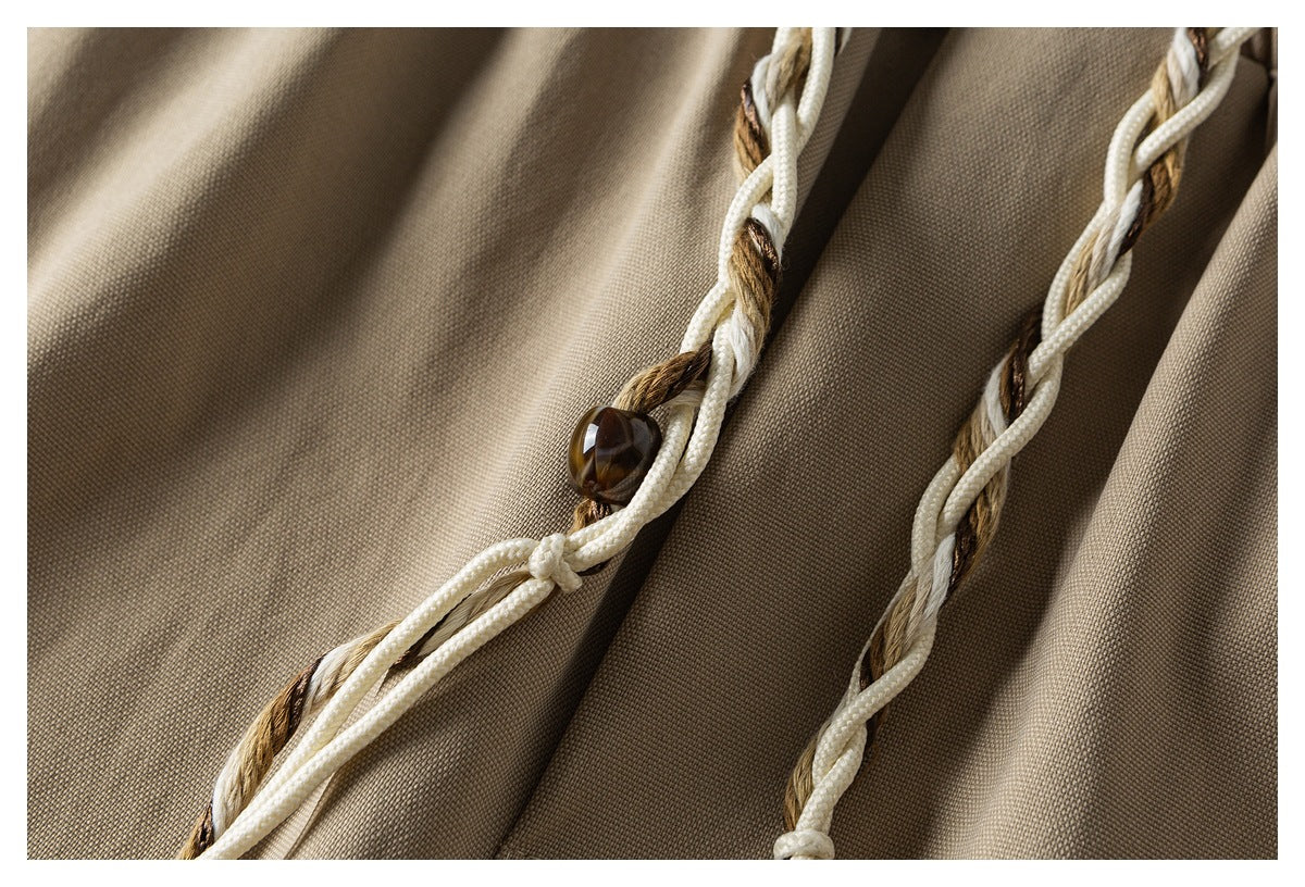 Close-up of khaki shorts with cream-and-brown braided drawstrings and a dark bead detail.