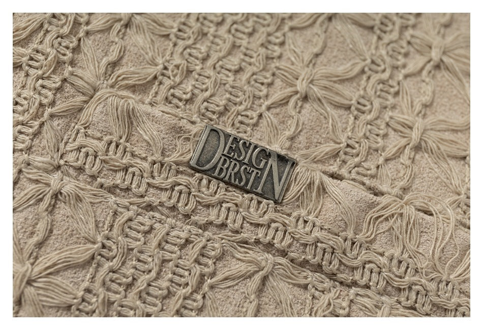 Close-up of beige raised floral stitching and ribbed bands around a small metal garment label.
