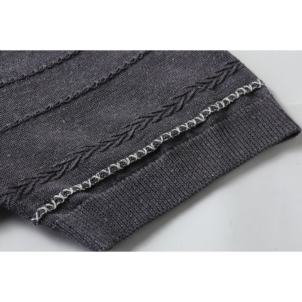 Close-up of a charcoal knit top's ribbed edge and contrasting looped stitching.
