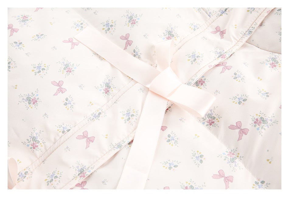 Close-up of a pale pink printed garment with a wide ribbon tie knotted over a piped edge.