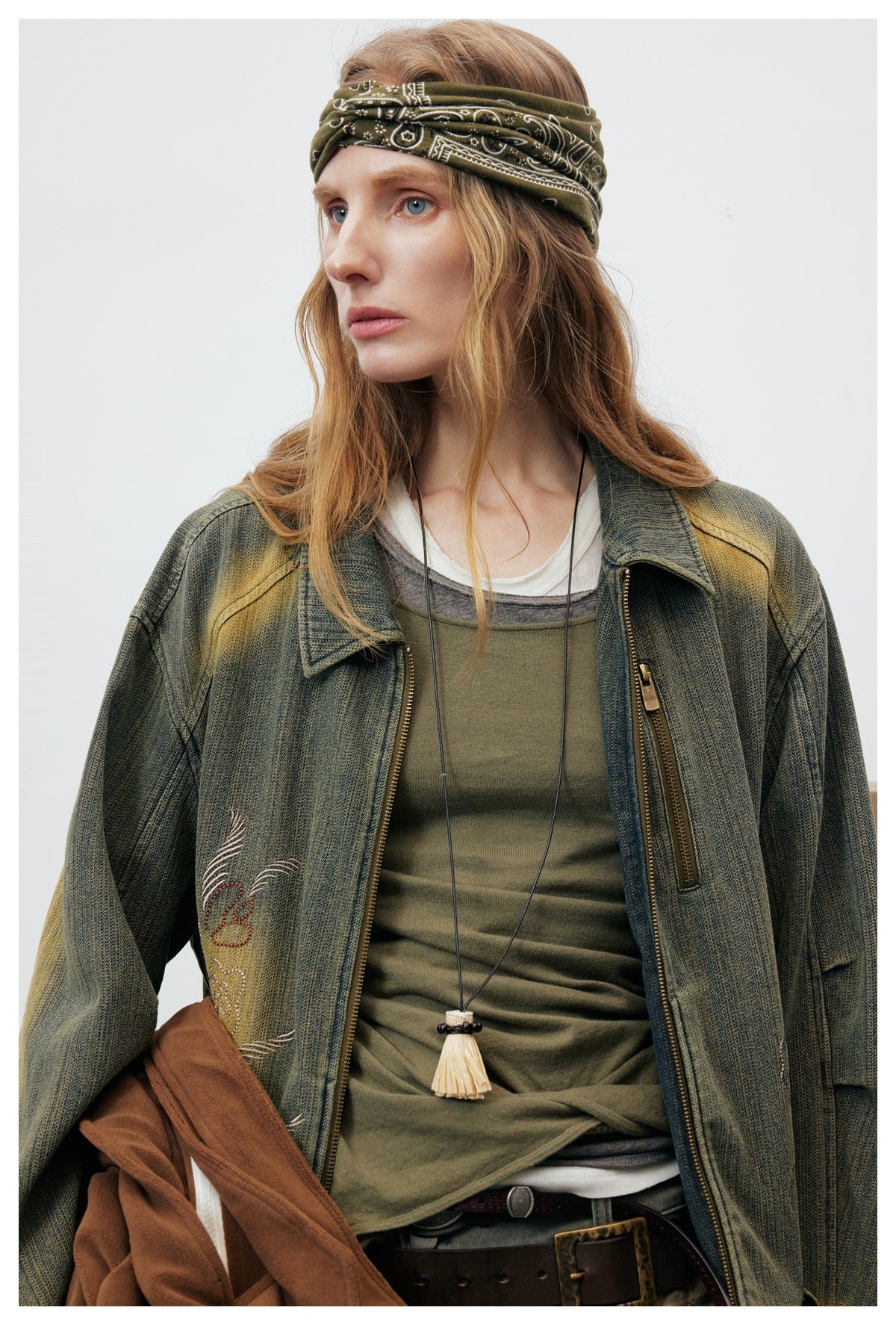 Close-up of a model wearing the faded denim jacket open with embroidery, zip chest pocket and collar visible