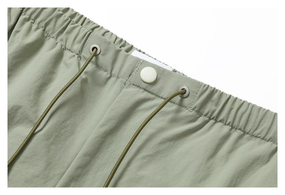 Close-up of sage pants showing the gathered elastic waistband, drawcord eyelets, and white snap closure.