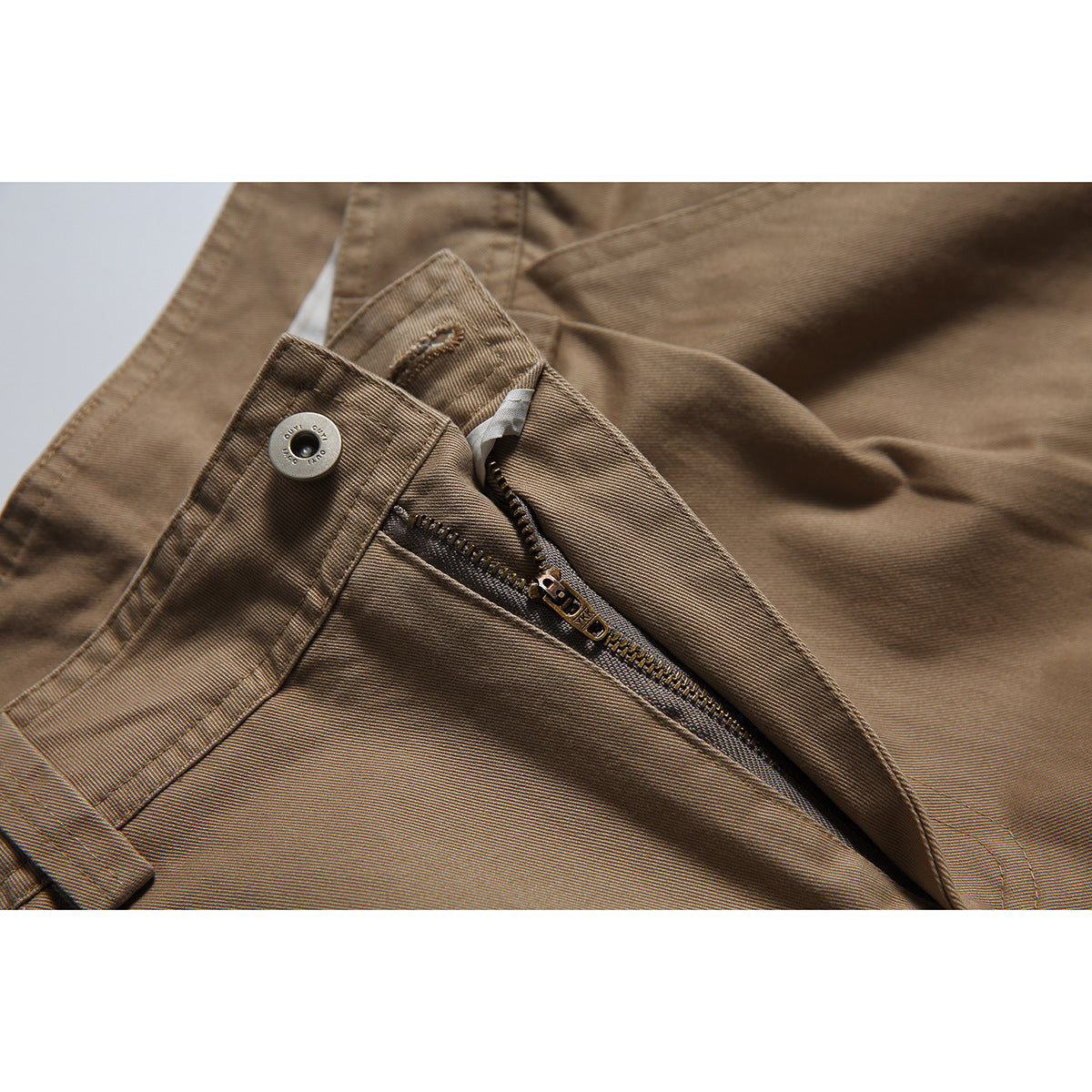 Close-up of brown trousers showing the waistband button, open zipper, stitching, and fabric texture.
