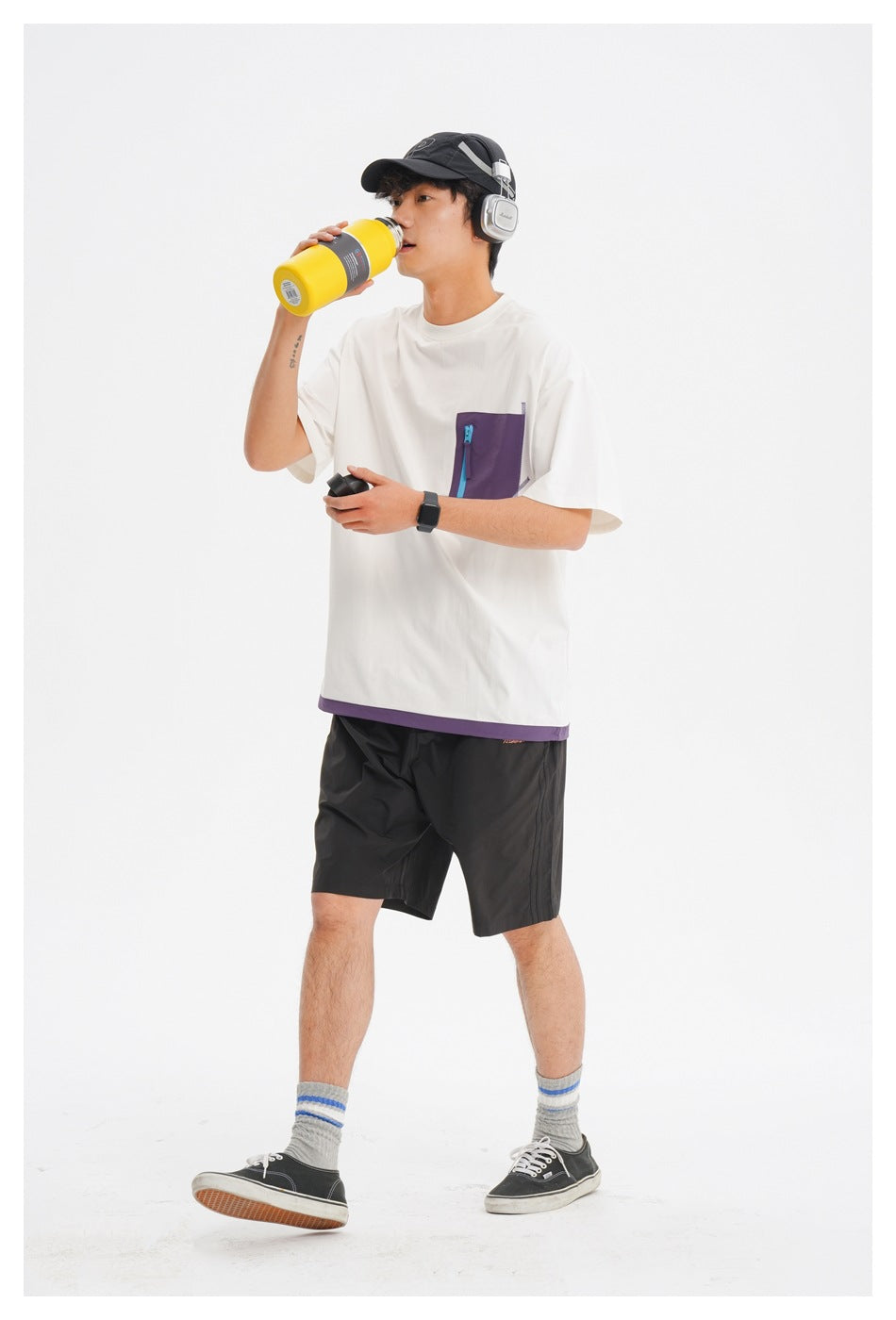 Model wearing a white oversized T-shirt with a purple zip pocket and hem trim, paired with black shorts.