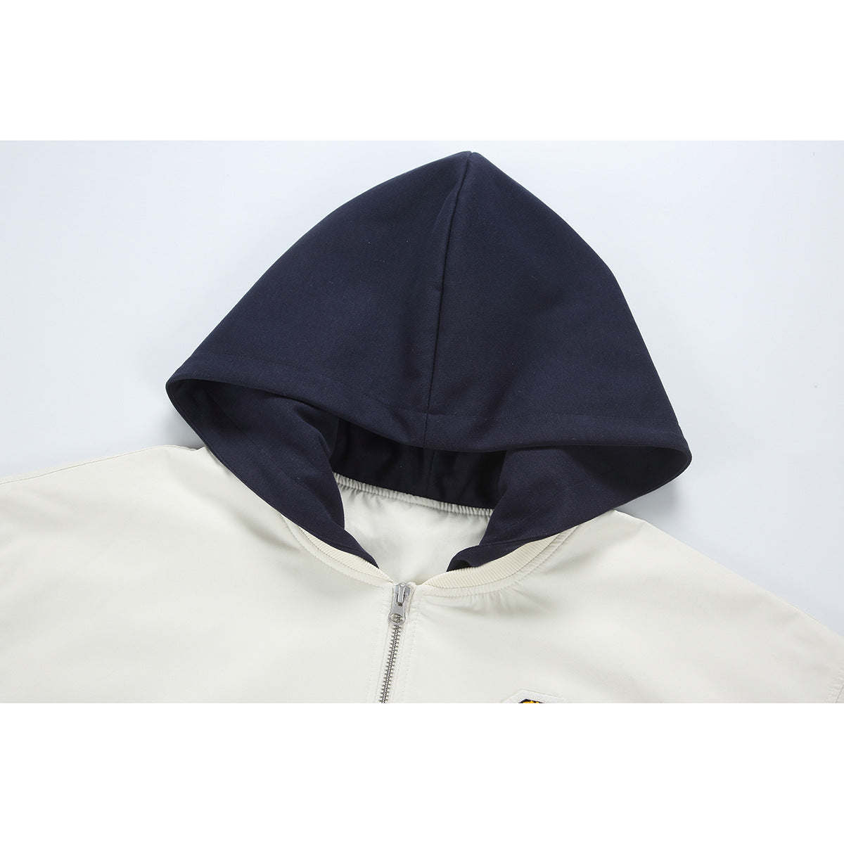 Close-up of a cream zip jacket with a large dark navy hood and ribbed neckline.