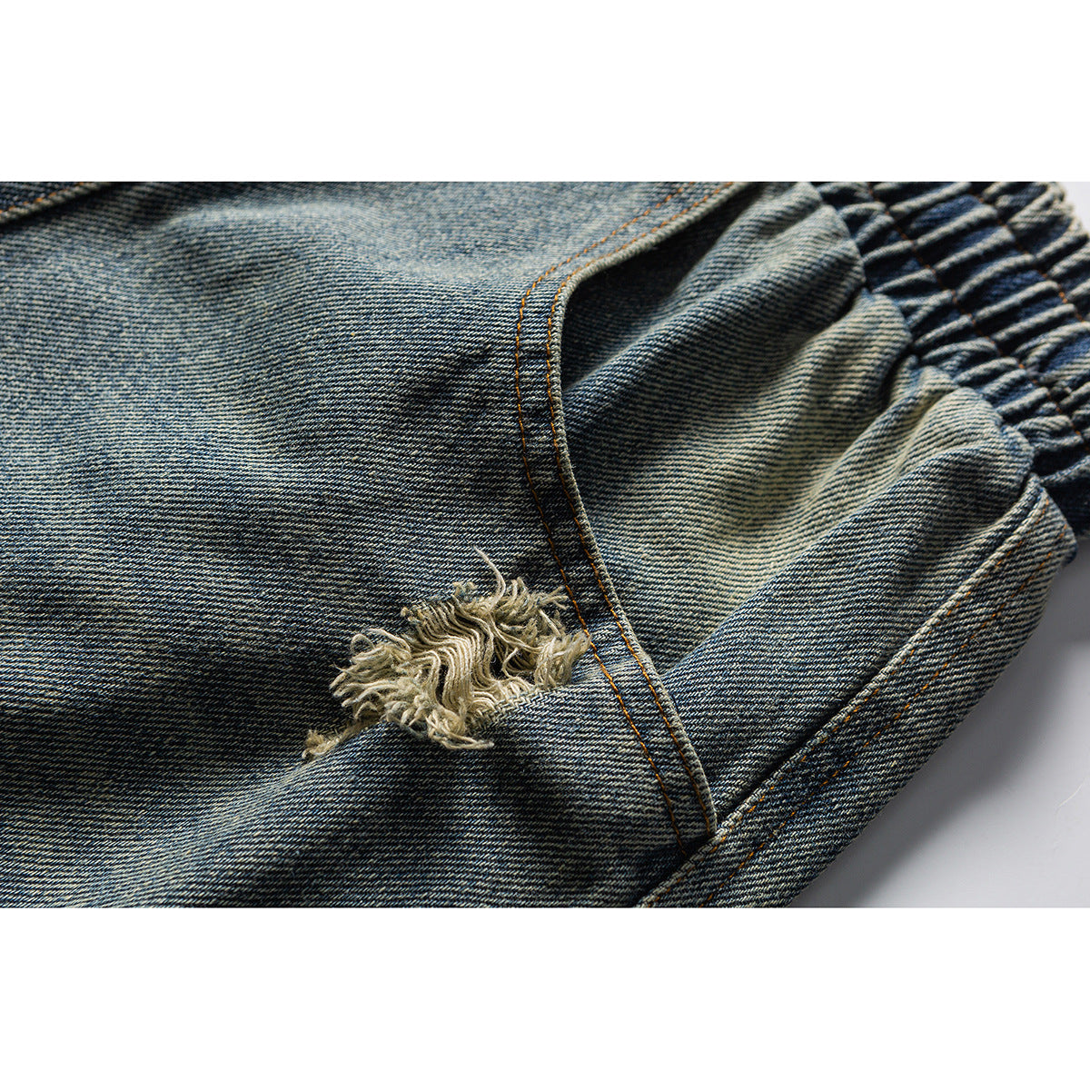 Close-up of blue denim shorts showing a distressed tear, orange stitching and part of the elastic waistband.