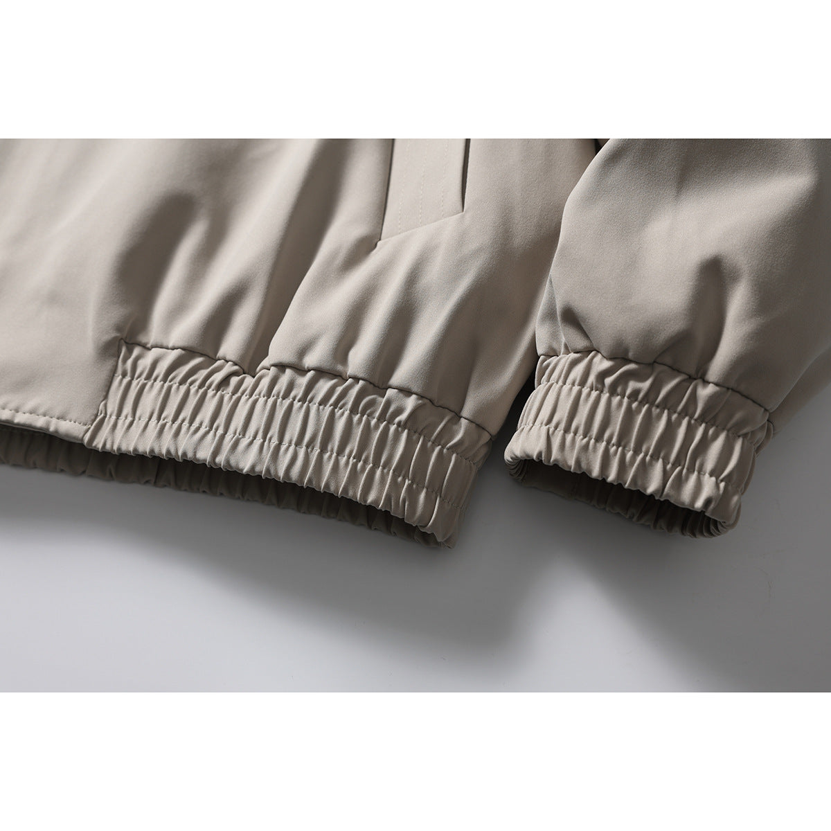 Close-up showing the light taupe jacket’s gathered elastic hem and sleeve cuffs.