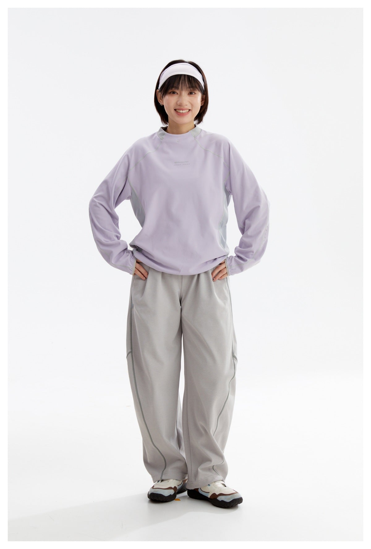 Full-length front view of a woman wearing a lavender long-sleeve top and loose gray pants.