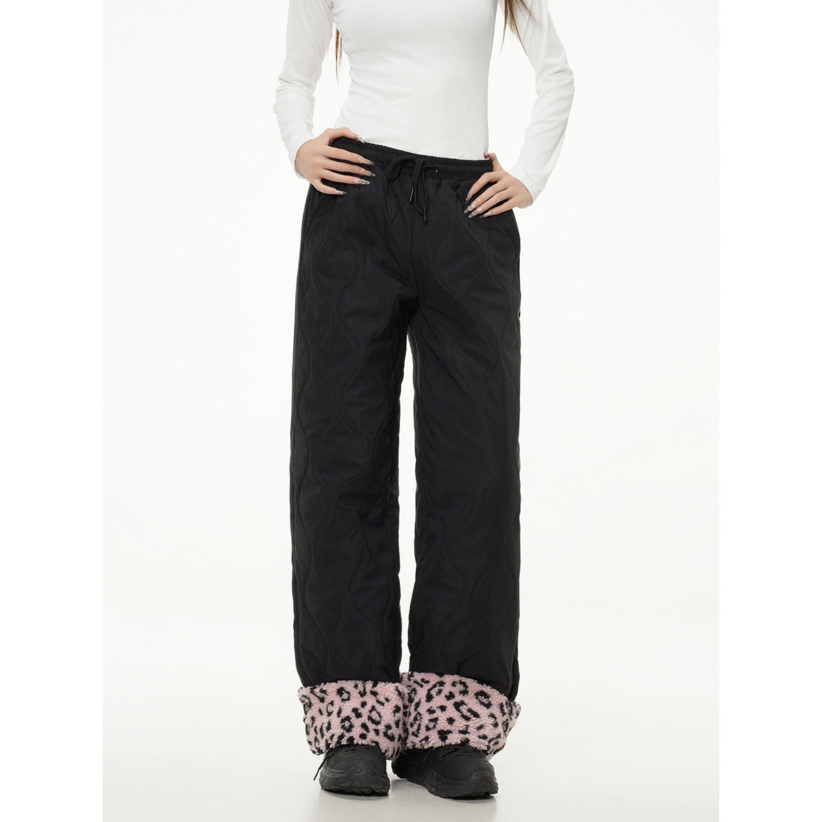 Front view of a model wearing black quilted wide-leg pants with a drawstring waist and pink leopard-print cuffs.