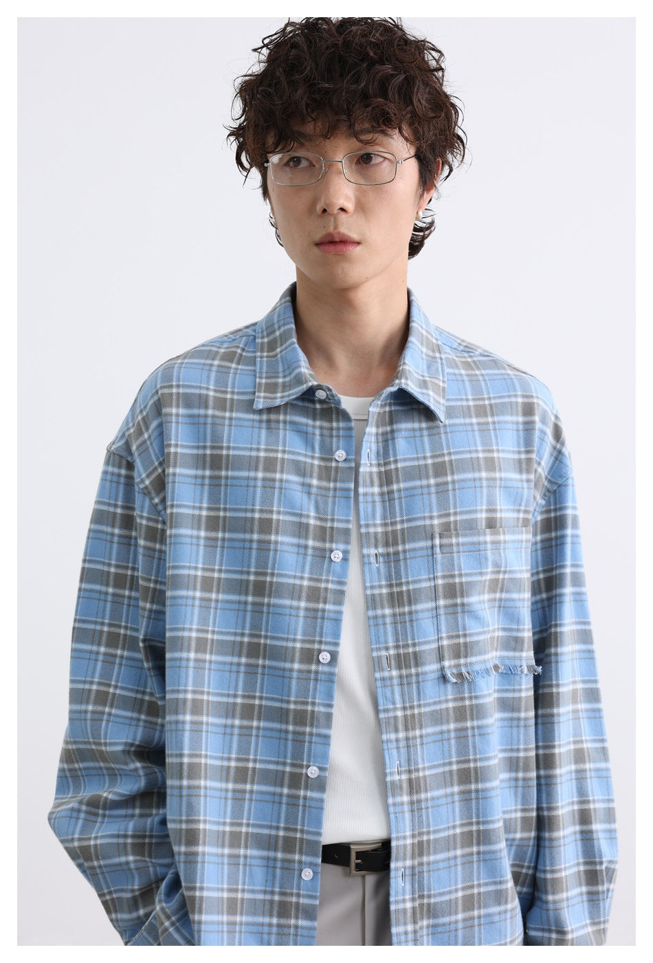 Close view of a model wearing a blue plaid button-up shirt with a frayed chest pocket edge.