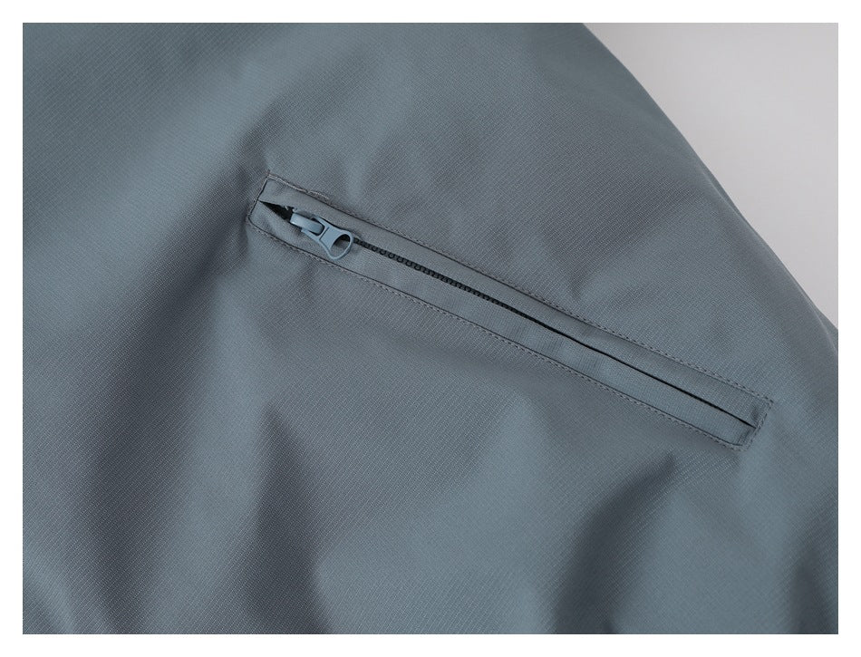 Close-up of a gray jacket's slanted zip pocket and zipper pull.