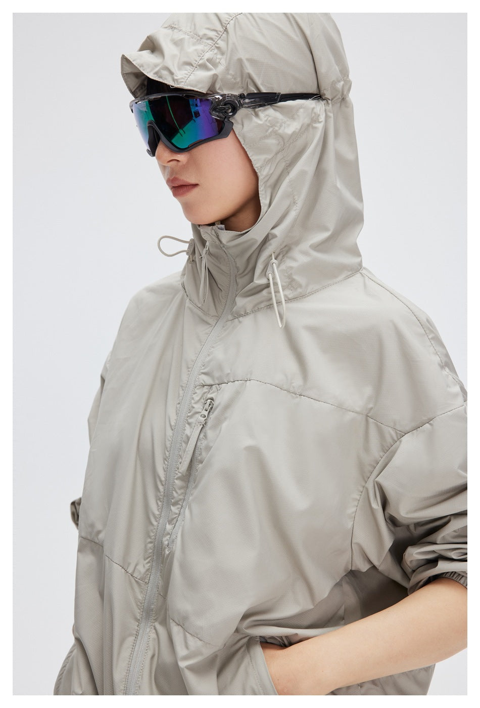 Side close-up of a model wearing a light gray hooded jacket with a zip chest pocket and drawcord hood.
