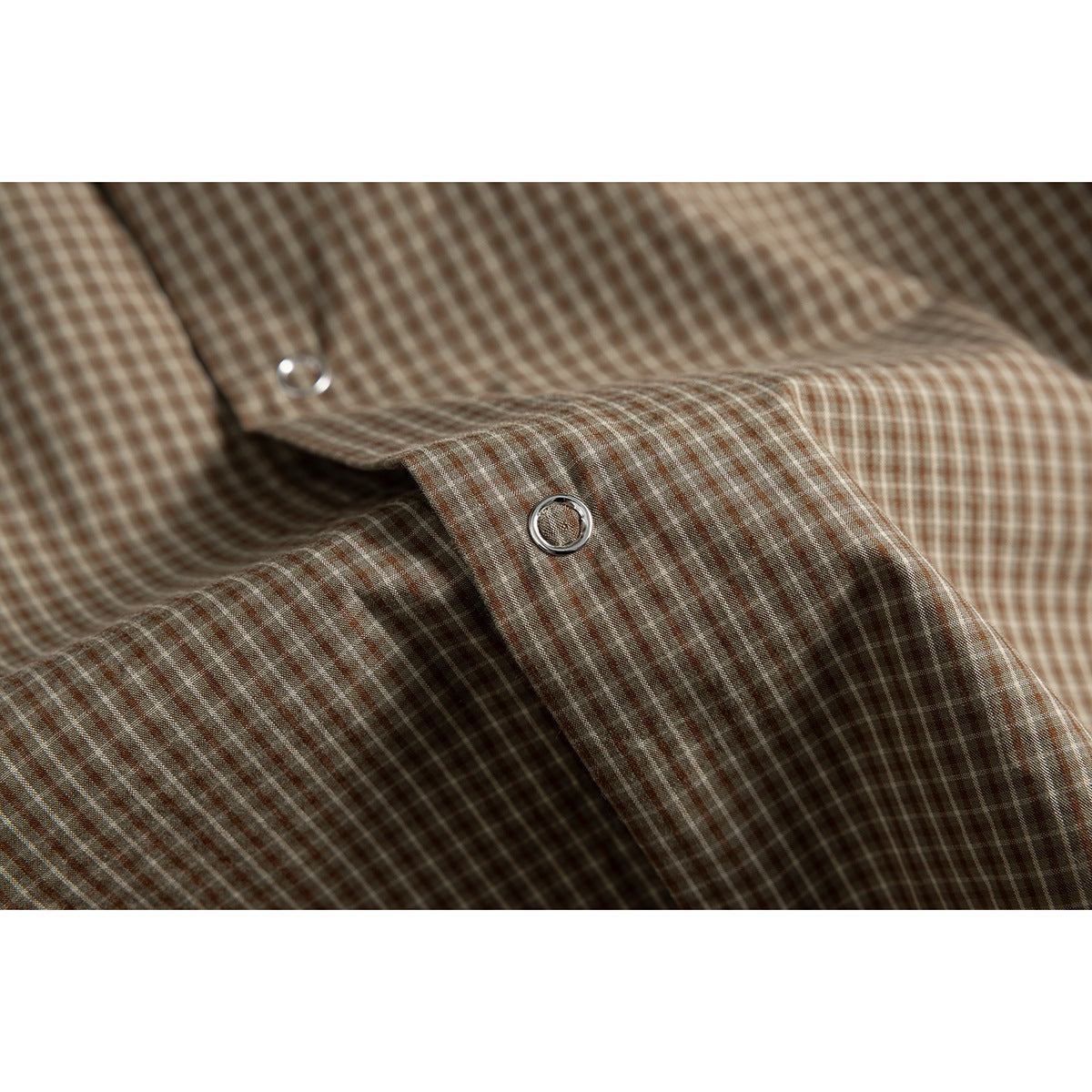 Close-up of a silver ring-style snap fastener on brown and beige checked shirt fabric.