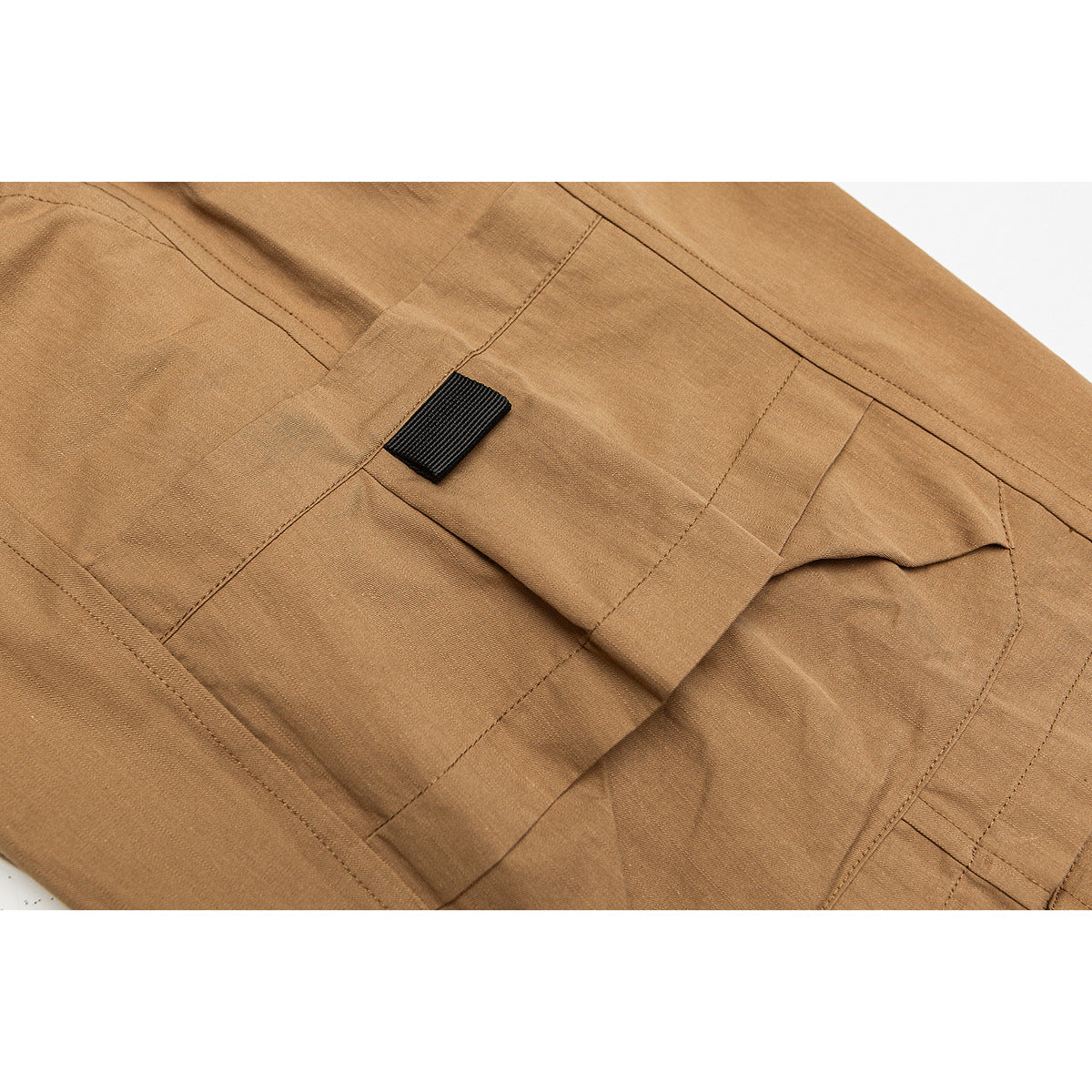 Close-up of tan cargo shorts showing a flap pocket, black fabric tab and stitched panels.