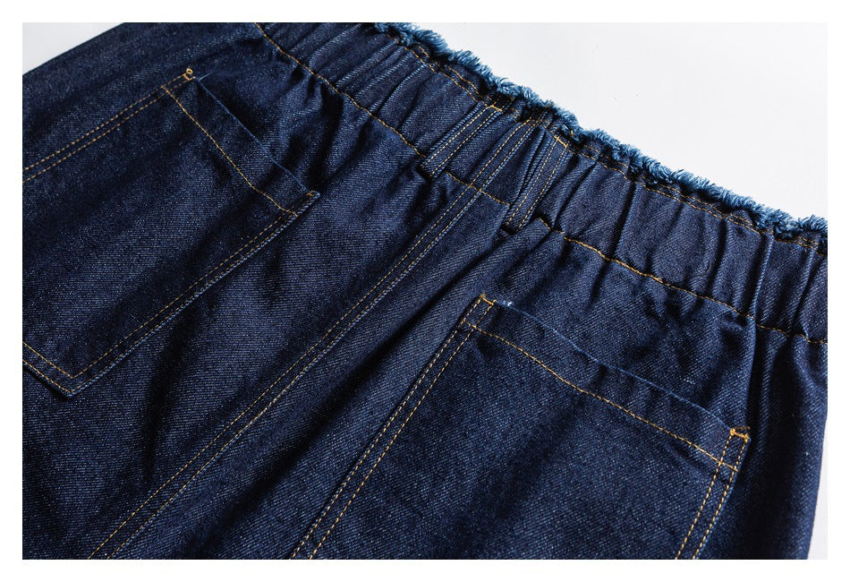 Close-up of the back of dark indigo denim pants, showing a gathered waistband and two stitched pockets.