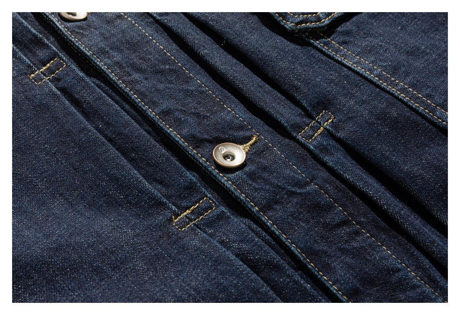Close-up of a dark indigo denim jacket front placket with a button, buttonholes, and contrast stitching.
