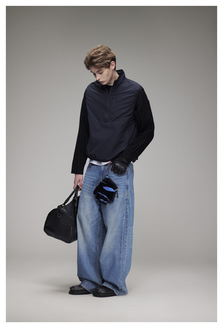 Model looking down in a navy quarter-zip pullover with black ribbed sleeves and wide-leg blue jeans.