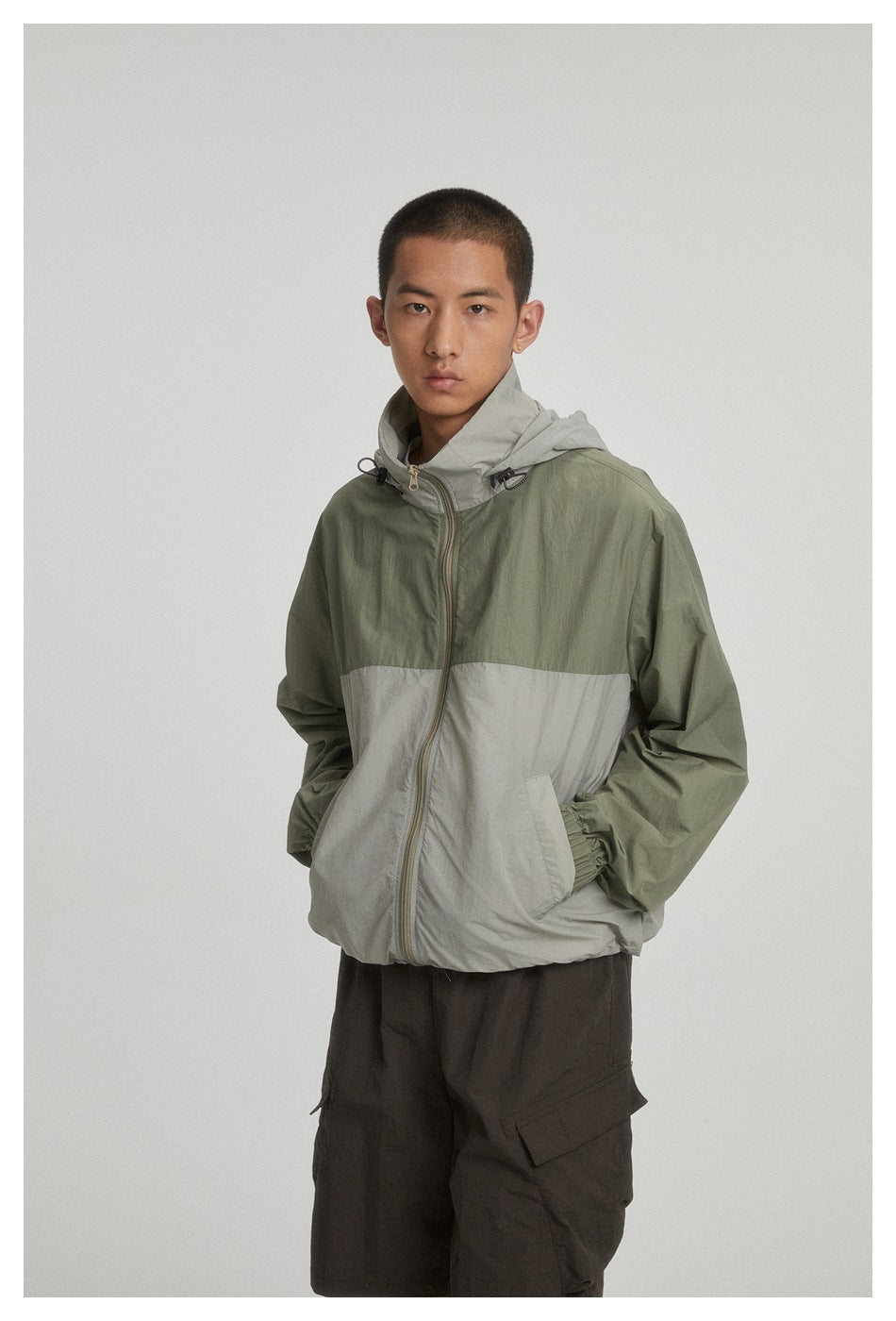 Model wearing a two-tone olive and light gray hooded zip jacket, shown from the front.