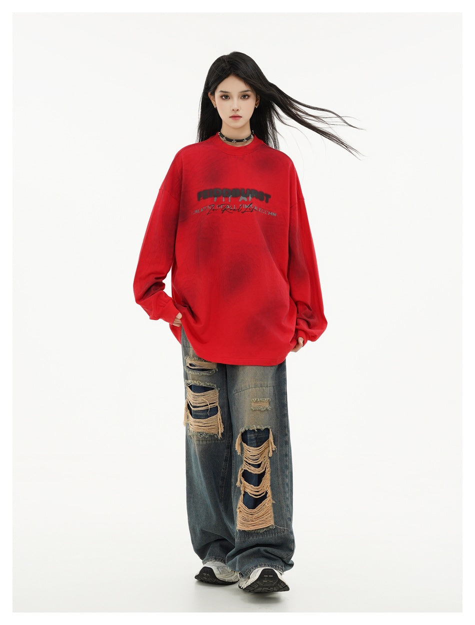 Model wearing an oversized red long-sleeve shirt with black chest lettering and distressed wide-leg jeans.