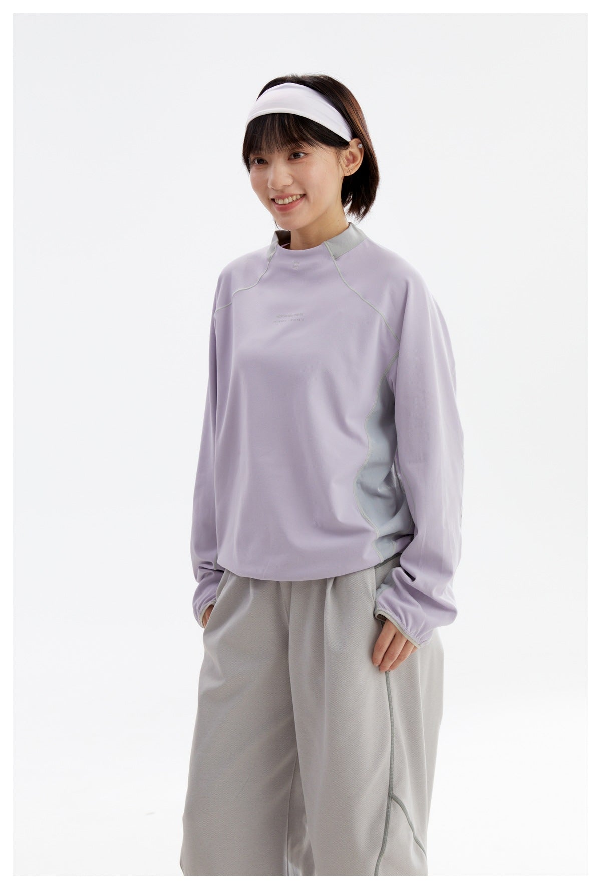 Angled view of a model wearing a lavender long-sleeve top with pale gray contrast panels and loose gray pants.