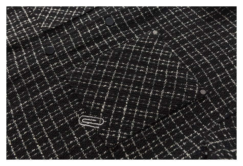 Close-up of the black-and-white plaid fabric, chest pocket, snap fasteners, and embroidered emblem.