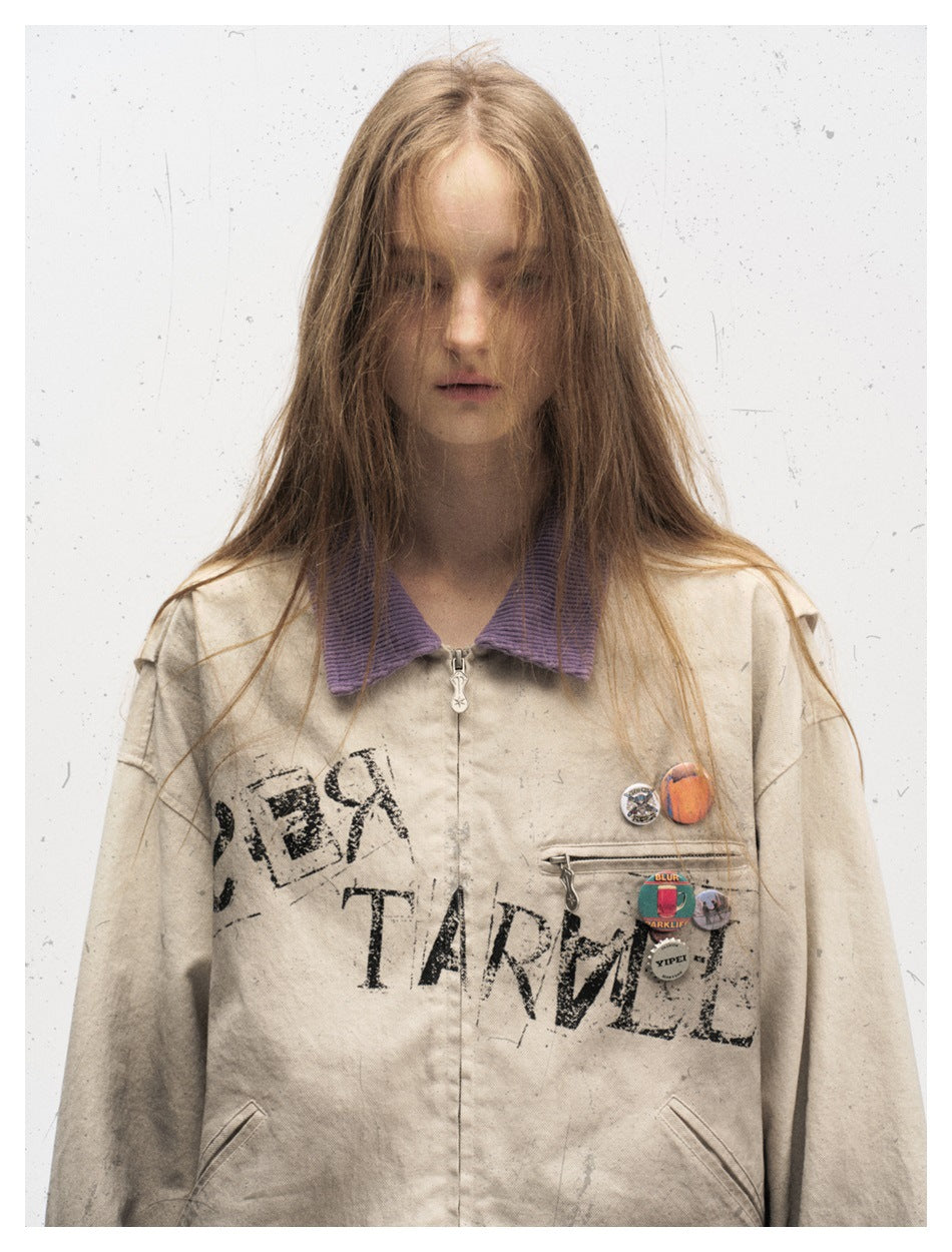 Front view of a model wearing a distressed beige jacket with a purple collar, black chest print, and decorative pins.