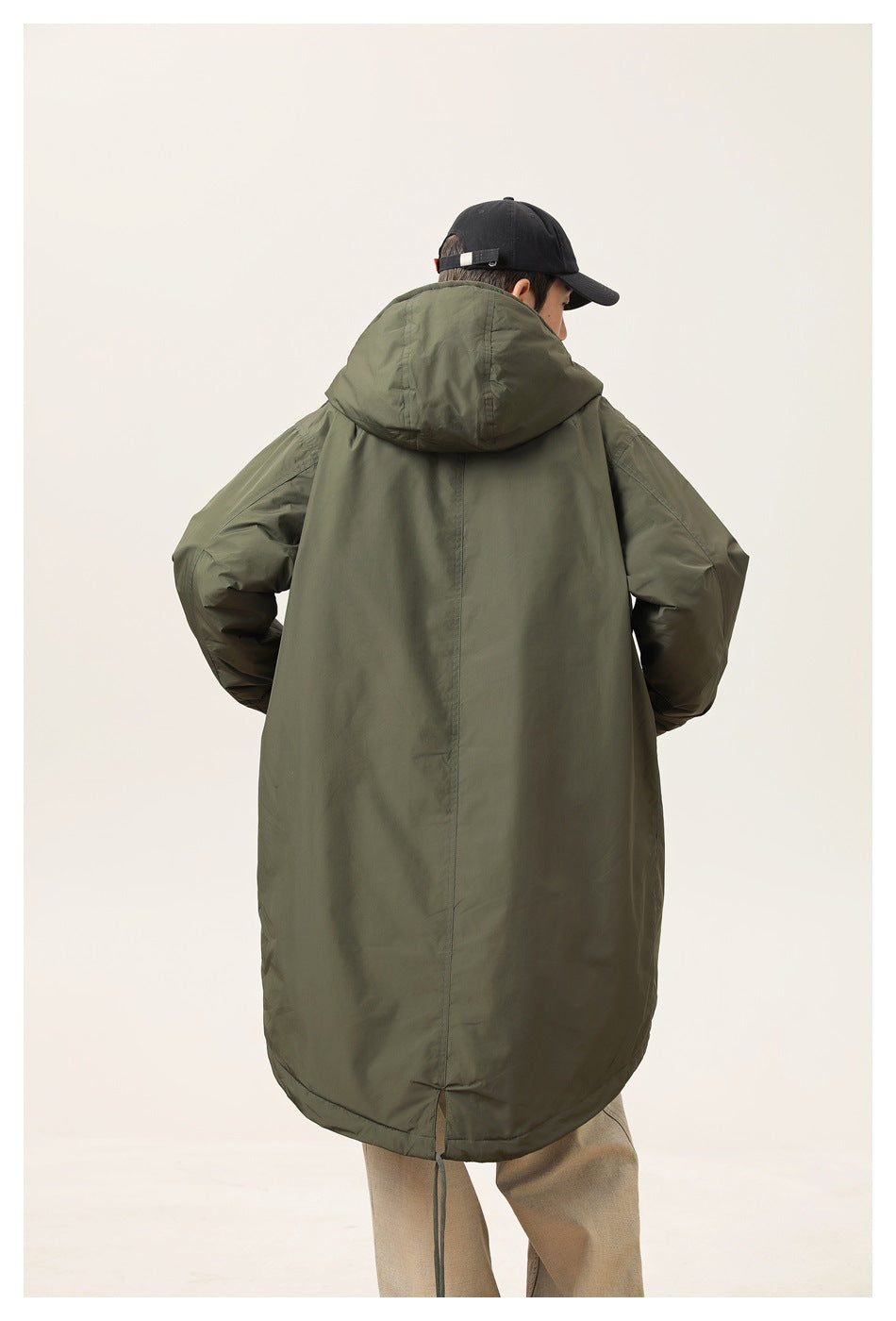 Rear view of a model wearing a long olive hooded parka with a rounded hem.